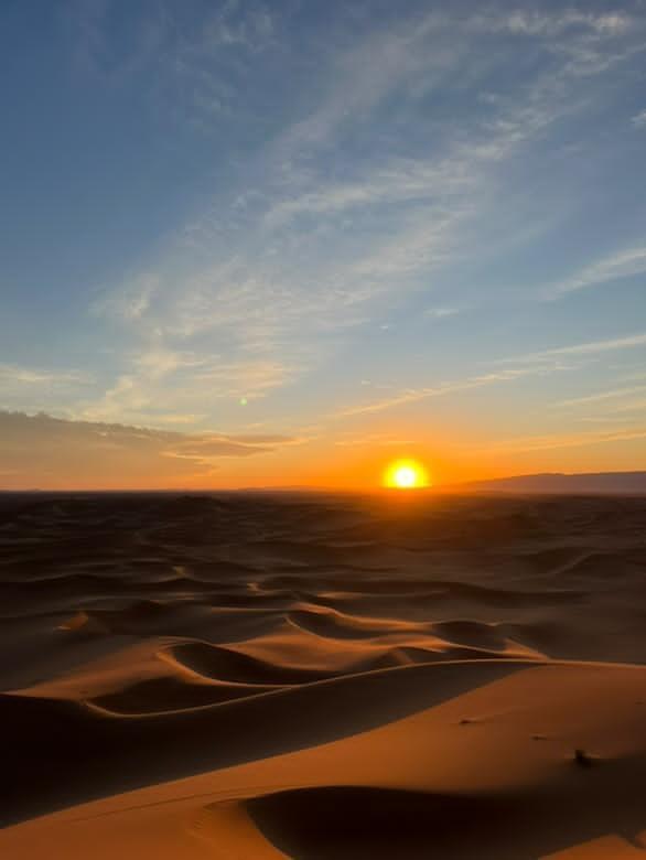 Expansive horizon where the golden Sahara dunes meet the blue sky near Foum Zguid, Morocco.